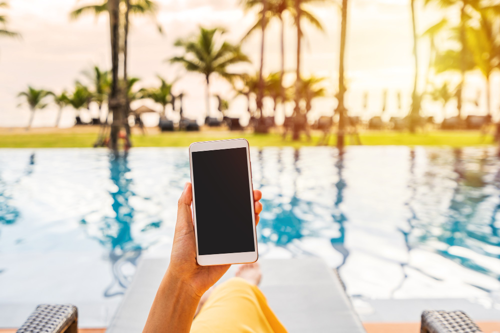 young-woman-traveler-relaxing-using-mobile-phone-by-hotel-pool-while-traveling-summer-vacation